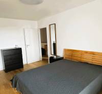 Ložnice v rodinném domě s postelí, komodou a podlahou s dřevěným dekorem.