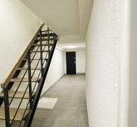 Chodba rodinného domu s minimalistickými schody, světlými stěnami a dlažbou.