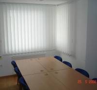Obchodní prostory s konferenčním stolem, modrými židlemi a vertikálními žaluziemi.