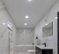 Koupelna v rodinném domě s keramickými stěnami a vanou, černým umyvadlem a zrcadlem.