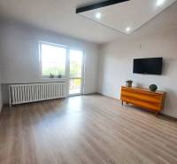 Obývací pokoj v rodinném domě s podlahou s dřevěným dekorem, televizí a komodou.