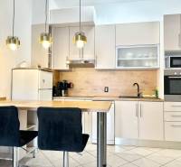 Kuchyně v rekreačním apartmánu s barovým pultem, závěsnými svítidly a bílou skříní.