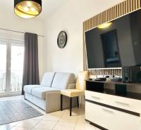 Obývací pokoj s pohovkou a televizorem v rekreačním apartmánu, světlá dlažba, balkónové dveře.