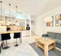 Rekreační apartmán s kuchyňským koutem, jídelním stolem, sedačkou a uměleckými obrazy na stěně.