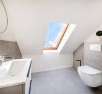 Světlá koupelna v podkroví s umyvadlem, toaletou a střešním oknem ve 2-pokojovém bytě.
