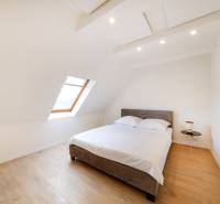 Světlá ložnice s postelí, střešním oknem a podlahou s dřevěným dekorem v 2pokojovém bytě.