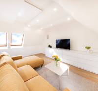 Obývací pokoj v 2-pokojovém bytě s béžovou sedačkou, bílým nábytkem a podlahou s dřevěným dekorem.