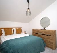 Ložnice v rekreačním apartmánu s postelí, dřevěnou komodou, zrcadlem a lampou.