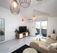 Obývací pokoj v rekreačním apartmánu s pohodlnou sedačkou, TV a balkonem.