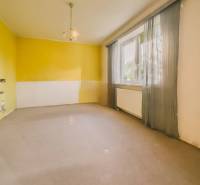 Pokoj v rodinném domě s velkým oknem, žluté stěny a závěsy.