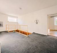 Interiér rodinného domu s kobercem, schodištěm a jednoduchou dekorací na stěně.