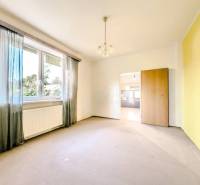 Pokoj s velkým oknem, radiátorem a průchodem v rodinném domě.