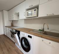 Kuchyně v 1-pokojovém bytě s bílou linkou, pračkou a podlahou s dřevěným dekorem.