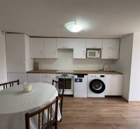 Kuchyně v 1-pokojovém bytě s bílými skříňkami a podlahou s dřevěným dekorem.