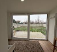 Pokoj jednopokojového bytu s výhledem na zahradu a podlahou s dřevěným dekorem.