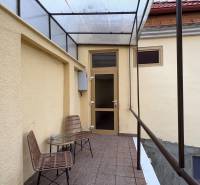 Krytá terasa se dvěma židlemi a stolkem před vstupem do garsonky.