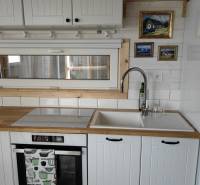 Kuchyňská linka v rodinném domě s bílými skříňkami, dřezem a vestavnou troubou.