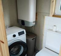 Koupelna v rodinném domě s pračkou, bojlerem a toaletou. Podlaha má dekorativní obklady.