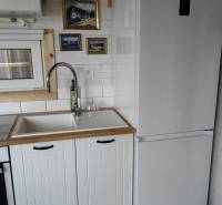 Kuchyně v rodinném domě s bílou linkou, lednicí a uměleckými obrazy na stěně.