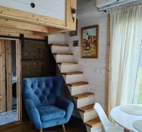 Interiér rodinného domu s modrým křeslem, dřevěným schodištěm a podlahou s dřevěným dekorem.