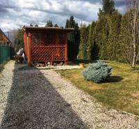 Dřevěná chata v Kráľovej nad Váhom s upravenou zahradou a keřem.