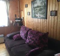 Stěna obložená dřevěnými panely s pohovkou, obrazem a poličkou v chatě.