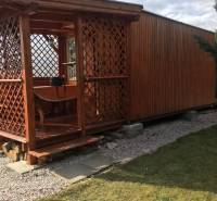 Dřevěná chata v Kráľovej nad Váhom s malou vyvýšenou terasou a trávníkem.