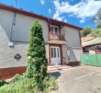 Rodinný dům v Tachtoch s bránou, terasou, balkónem a okolím se zelení.