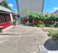 Rodinný dům v Tachtoch s dvorem, betonovou plochou, zelení, plotem a garážovými dveřmi.