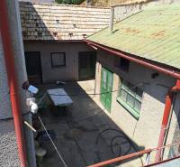 Dvůr rodinného domu v Tachtoch s viditelnými dveřmi, stolem a travnatým svahem.