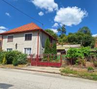 Rodinný dům v Tachtoch, s červenou střechou, plotem a zahradou v zeleném prostředí.