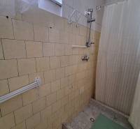 Koupelna v rodinném domě s keramickými obklady a závěsem nad sprchovým koutem.