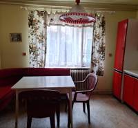 Kuchyně v rodinném domě s červeným nábytkem, barevnými závěsy a plastovými židlemi.