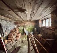 Suterén rodinného domu s cihlovými stěnami a stropem, uskladněné trubky a nářadí.