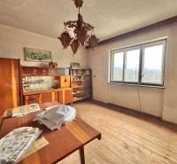 Pokoj v rodinném domě s dřevěným dekorem, vintage nábytkem, lustrem a velkým oknem.