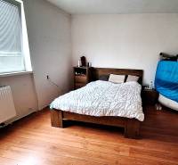 Ložnice v rodinném domě s postelí, komodou a podlahou s dřevěným dekorem.