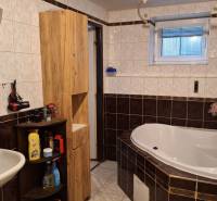 Koupelna s rohovou vanou, bílým umyvadlem a dřevěným nábytkem v rodinném domě.