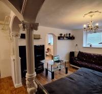 Obývací pokoj v rodinném domě s pohovkou, skleněným stolem a sloupy.