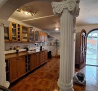 Interiér rodinného domu s dřevěnou kuchyňskou linkou, sloupy a podlahou s dřevěným dekorem.