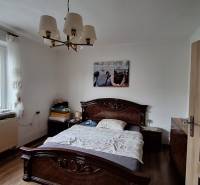 Ložnice v rodinném domě s postelí, lustrem a podlahou s dřevěným dekorem.