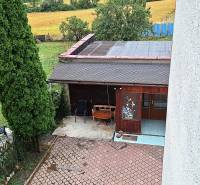 Zahrada rodinného domu v Zacharovcích s altánkem, stromy a výhledem na pole.