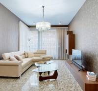 Obývací pokoj v 3-pokojovém bytě s béžovou sedačkou, skleněným stolem a televizorem.