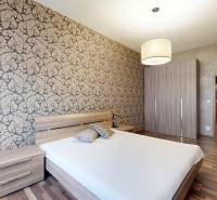 Ložnice v 3-pokojovém bytě s vzorovanou tapetou a podlahou s dřevěným dekorem.