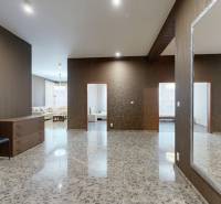 Prostorná chodba s dlažbou, zrcadlem, dvěma židlemi a výhledem do obývacího pokoje.