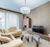 Obývací pokoj v 3-pokojovém bytě s béžovou sedačkou, vzorovanou stěnou a skleněným stolkem.