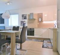 Moderní kuchyně s jídelním stolem, bílými skříňkami a podlahou s dřevěným dekorem v 2pokojovém bytě.