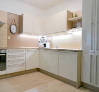 Kuchyně v 2-pokojovém bytě s bílými skříňkami a podlahou s dřevěným dekorem.