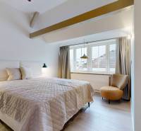 Ložnice se světlou podlahou s dřevěným dekorem, velkým oknem a pohodlným křeslem.