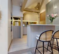 Interiér 4-pokojového bytu s barovými židlemi, dekorativní stěnou a květinami ve váze.