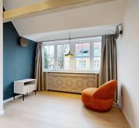 Pokoj ve 4pokojovém bytě s oranžovým křeslem, světlou podlahou s dřevěným dekorem a velkým oknem.